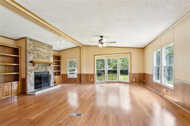 12175 Reid Rd, Amite, LA 70422 - unfurnished living room featuring a textured ceiling, wood finished floors, a ceiling fan, a fireplace, and wainscoting
