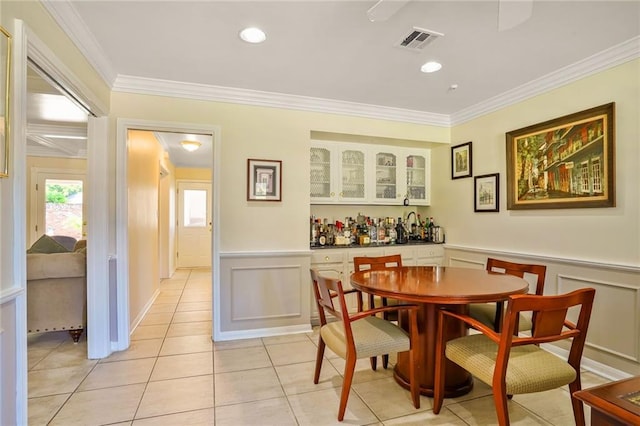 2442 Killdeer St, New Orleans, LA 70122 - dining space with crown molding, light tile patterned floors, a decorative wall, wainscoting, and a bar