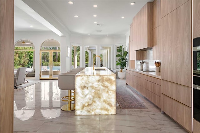 139 Fontainbleau Dr, Mandeville, LA 70471 - kitchen with modern cabinets, light marble finish floors, light brown cabinets, crown molding, and a kitchen island with sink