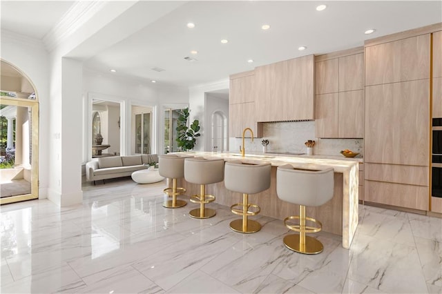 139 Fontainbleau Dr, Mandeville, LA 70471 - kitchen featuring light brown cabinets, modern cabinets, light marble finish floors, a kitchen breakfast bar, and recessed lighting