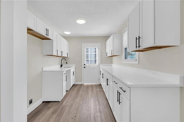 6073 Wickfield Dr, New Orleans, LA 70122 - kitchen featuring a sink, light wood-style flooring, baseboards, light countertops, and a textured ceiling