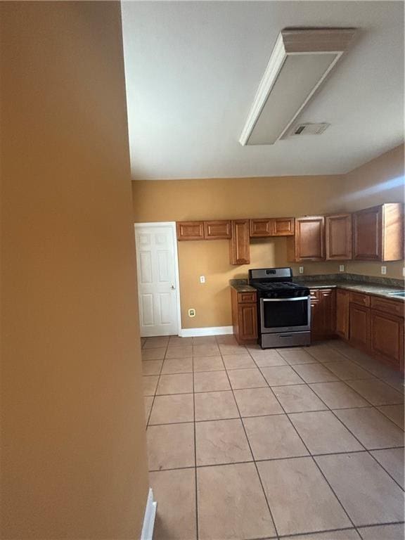 2428 Hamilton St, New Orleans, LA 70118 - kitchen with stainless steel gas range, light tile patterned floors, brown cabinets, baseboards, and dark countertops