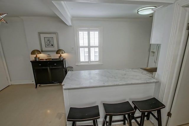 1323 Dauphine St Unit 3, New Orleans, LA 70116 - kitchen with a peninsula, light stone countertops, a breakfast bar, ornamental molding, and white cabinetry