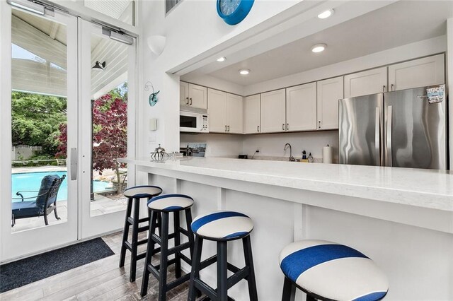 105 Mulberry Dr, Metairie, LA 70005 - kitchen featuring freestanding refrigerator, white microwave, wood finished floors, a breakfast bar, and light countertops