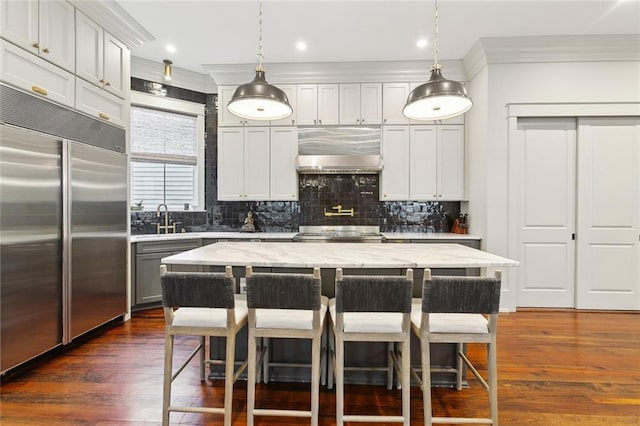 1026 Valence St, New Orleans, LA 70115 - kitchen with stainless steel built in refrigerator, exhaust hood, crown molding, a sink, and a breakfast bar area