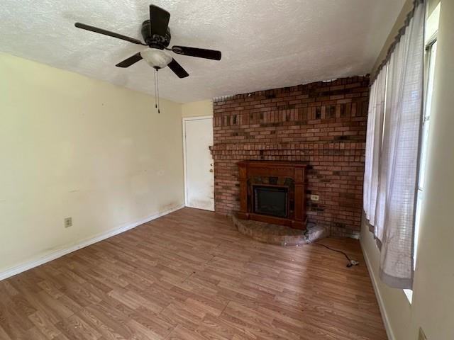 44373 Elmer Magee Rd, Franklinton, LA 70438 - unfurnished living room featuring a textured ceiling, baseboards, wood finished floors, a fireplace, and a ceiling fan