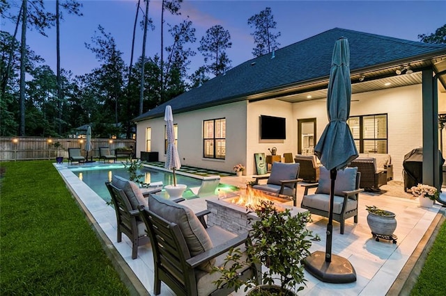 121 Chateau Papillon Ln, Mandeville, LA 70471 - back of property at dusk featuring a shingled roof, a patio area, stucco siding, and an outdoor living space with a fire pit