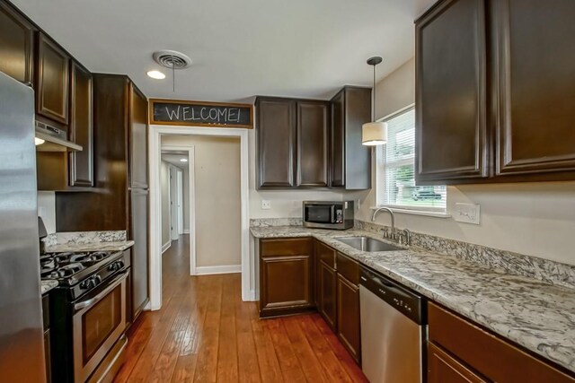 3617 Tartan Dr, Metairie, LA 70003 - kitchen with appliances with stainless steel finishes, under cabinet range hood, dark wood-type flooring, light stone counters, and decorative light fixtures