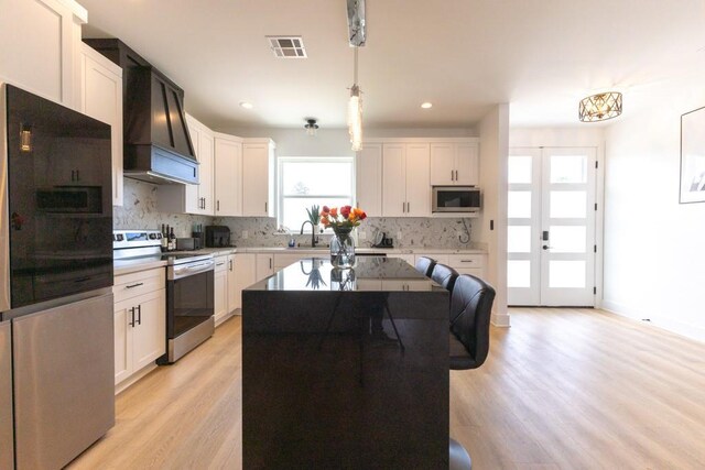 322 Spartan Loop, Slidell, LA 70458 - kitchen featuring appliances with stainless steel finishes, custom range hood, light wood-type flooring, backsplash, and decorative light fixtures