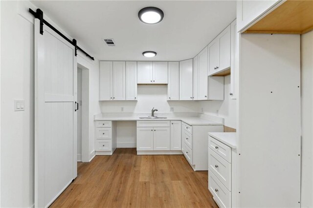 35210 Windsor Dr, Slidell, LA 70460 - kitchen with a sink, light wood-style flooring, white cabinets, a barn door, and light countertops