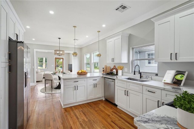 2327 Pauline St, New Orleans, LA 70117 - kitchen featuring appliances with stainless steel finishes, a peninsula, white cabinets, light wood finished floors, and recessed lighting