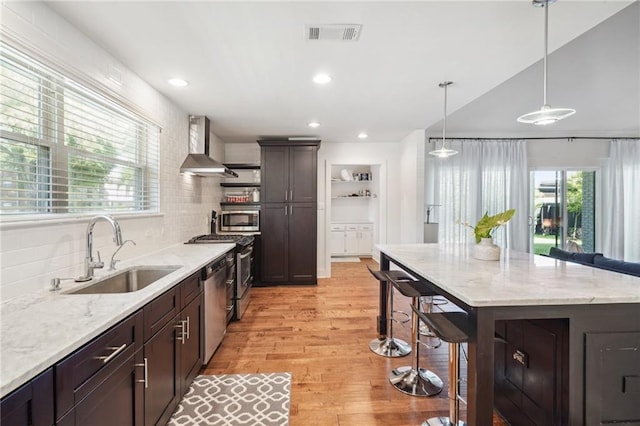 5727 Fleur De Lis Dr, New Orleans, LA 70124 - kitchen featuring a sink, wall chimney range hood, appliances with stainless steel finishes, a kitchen breakfast bar, and light wood-style floors