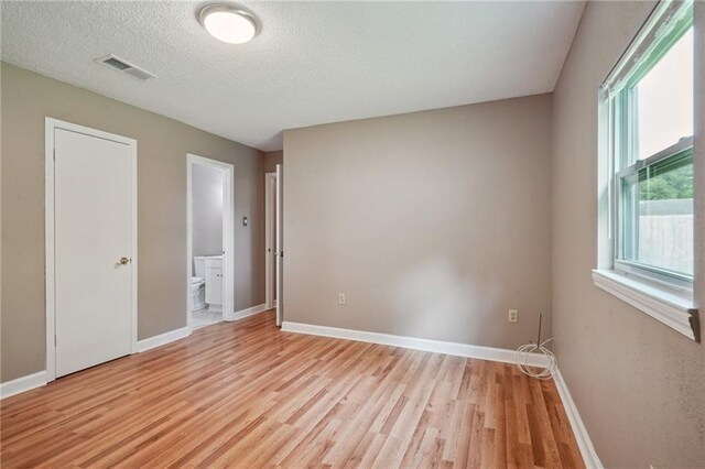 4124 Ames Blvd, Marrero, LA 70072 - unfurnished bedroom with light wood finished floors, baseboards, connected bathroom, and a textured ceiling