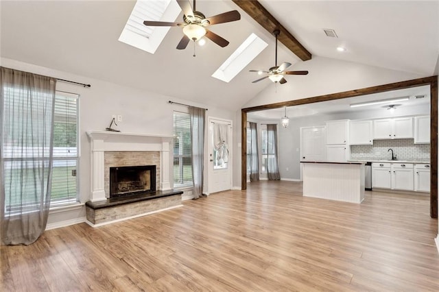 185 Lark St, Slidell, LA 70460 - unfurnished living room featuring ceiling fan, beam ceiling, a skylight, light wood finished floors, and a stone fireplace