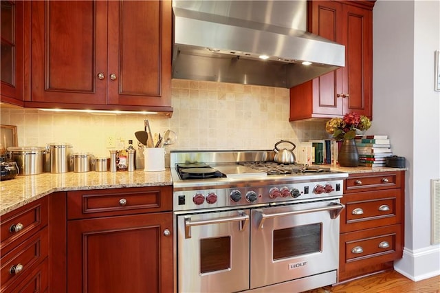 826 N Carrollton Ave, New Orleans, LA 70119 - kitchen featuring range with two ovens, wall chimney range hood, reddish brown cabinets, and tasteful backsplash