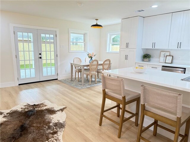 4413 Napoli Dr, Metairie, LA 70002 - kitchen featuring french doors, dishwasher, light wood-type flooring, a kitchen breakfast bar, and white cabinets