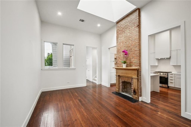2417 Rousseau St, New Orleans, LA 70130 - unfurnished living room featuring dark wood-type flooring, baseboards, a large fireplace, a towering ceiling, and recessed lighting