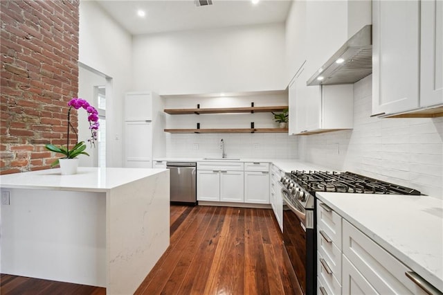 2417 Rousseau St, New Orleans, LA 70130 - kitchen featuring appliances with stainless steel finishes, wall chimney range hood, open shelves, dark wood finished floors, and recessed lighting