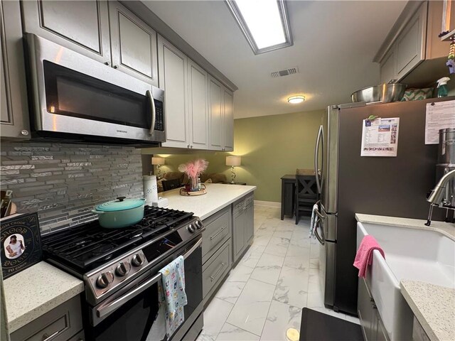 5121 Pike Dr, Metairie, LA 70003 - kitchen featuring stainless steel appliances, light marble finish flooring, tasteful backsplash, and gray cabinetry
