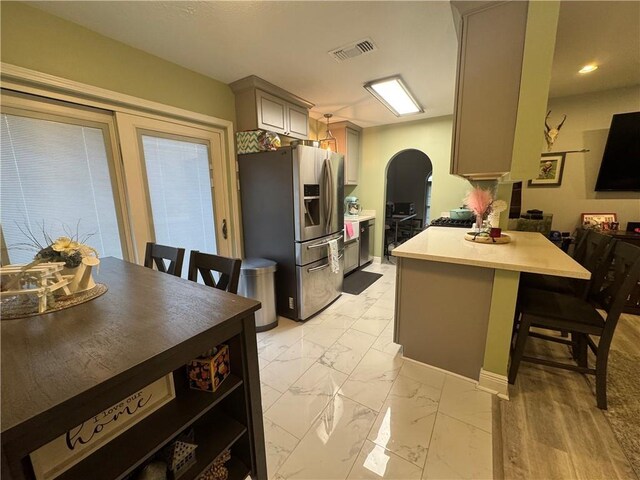 5121 Pike Dr, Metairie, LA 70003 - kitchen featuring stainless steel fridge with ice dispenser, a peninsula, light marble finish flooring, a breakfast bar area, and light countertops