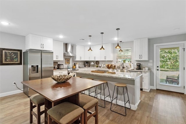 23375 Lowe Davis Rd, Covington, LA 70435 - kitchen featuring wall chimney exhaust hood, appliances with stainless steel finishes, light wood-type flooring, white cabinets, and a kitchen island