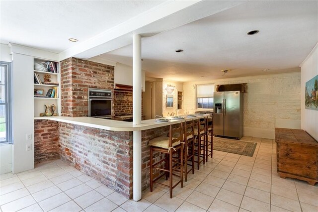 212 Linton Ave, Natchez-Ms, MS 39120 - kitchen with stainless steel appliances, light tile patterned floors, healthy amount of natural light, a kitchen breakfast bar, and brick wall