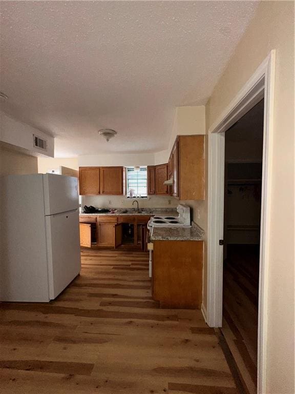 70915 S Gayoso St, New Orleans, LA 70119 - kitchen with freestanding refrigerator, brown cabinets, light wood-style flooring, a textured ceiling, and under cabinet range hood