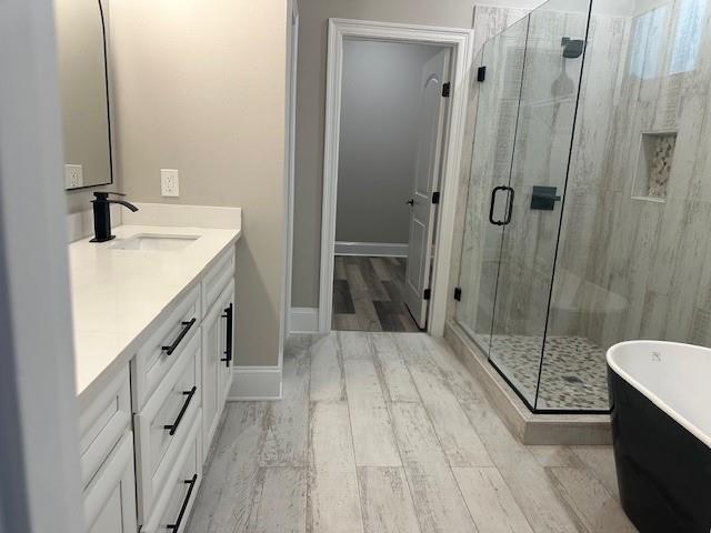 1731 Pratt Dr, New Orleans, LA 70122 - bathroom featuring double vanity, a stall shower, a freestanding bath, wood finished floors, and baseboards