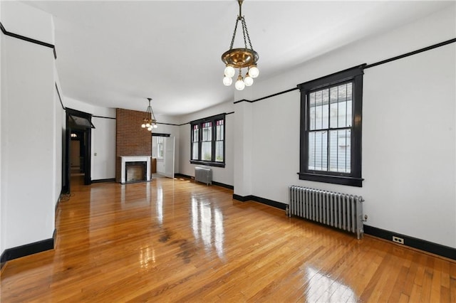 1311 Bourbon St, New Orleans, LA 70116 - unfurnished living room featuring radiator heating unit, a chandelier, a brick fireplace, light wood-style floors, and baseboards