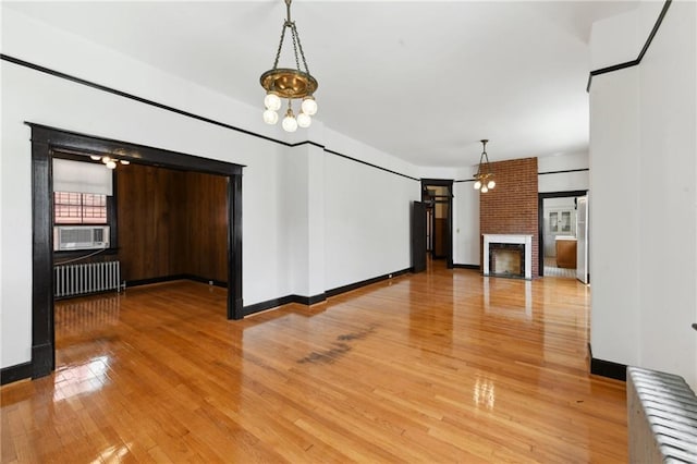 1311 Bourbon St, New Orleans, LA 70116 - unfurnished living room with radiator heating unit, a fireplace, light wood-style floors, and a chandelier