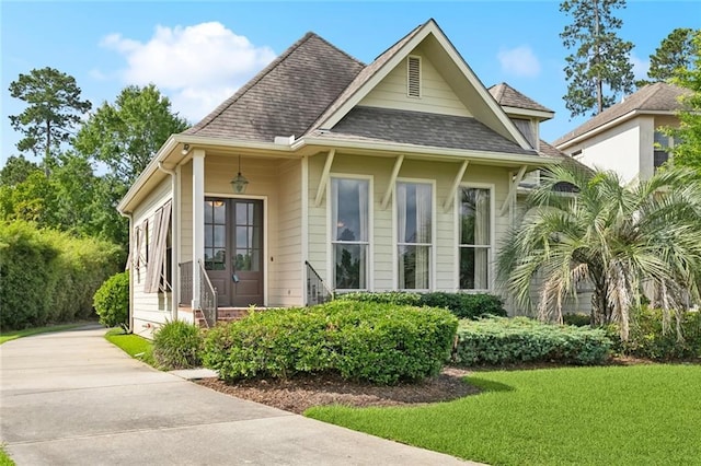 view of front of house with a front yard, roof with shingles, concrete driveway, and french doors