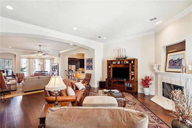 living area with arched walkways, a ceiling fan, a premium fireplace, dark wood-style floors, and ornamental molding