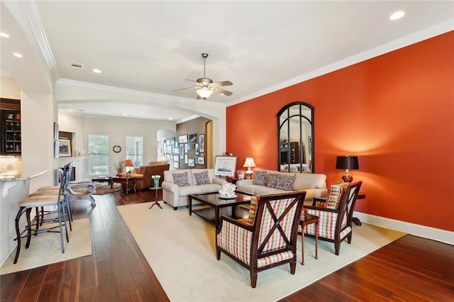 living area featuring arched walkways, dark wood-type flooring, a ceiling fan, ornamental molding, and recessed lighting