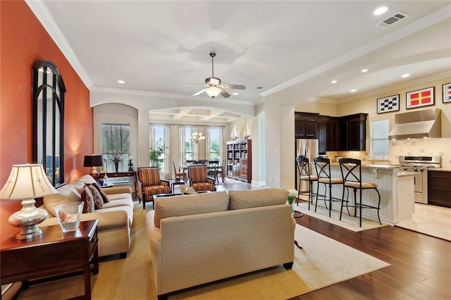 living room featuring ornamental molding, arched walkways, a ceiling fan, light wood-type flooring, and recessed lighting