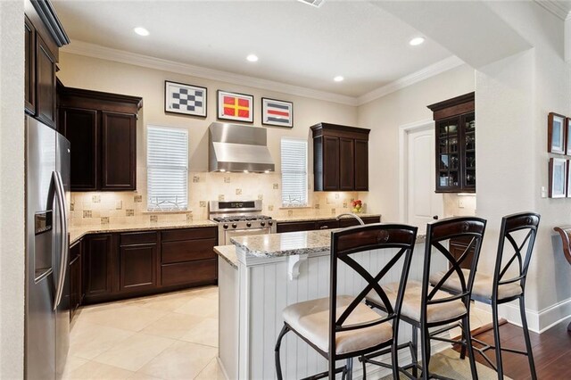 kitchen featuring stainless steel appliances, wall chimney range hood, a kitchen breakfast bar, decorative backsplash, and ornamental molding