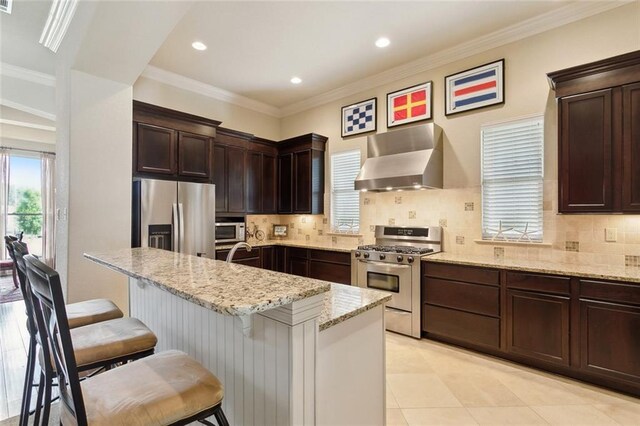 kitchen with stainless steel appliances, wall chimney exhaust hood, light stone countertops, tasteful backsplash, and crown molding