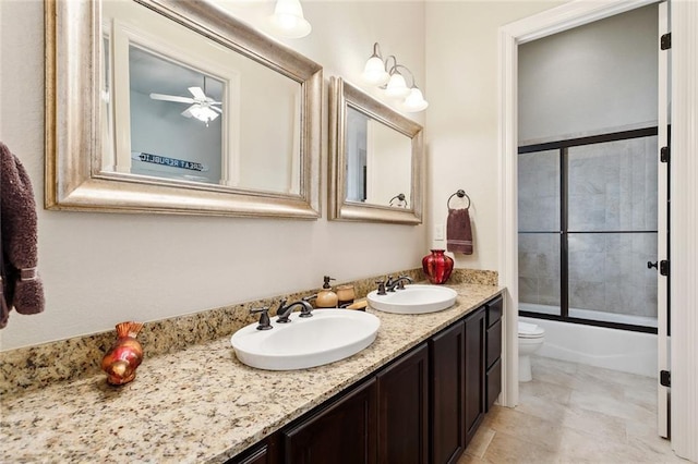 bathroom featuring double vanity, toilet, combined bath / shower with glass door, and a ceiling fan