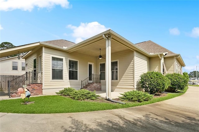 view of side of home featuring a ceiling fan, a lawn, and roof with shingles