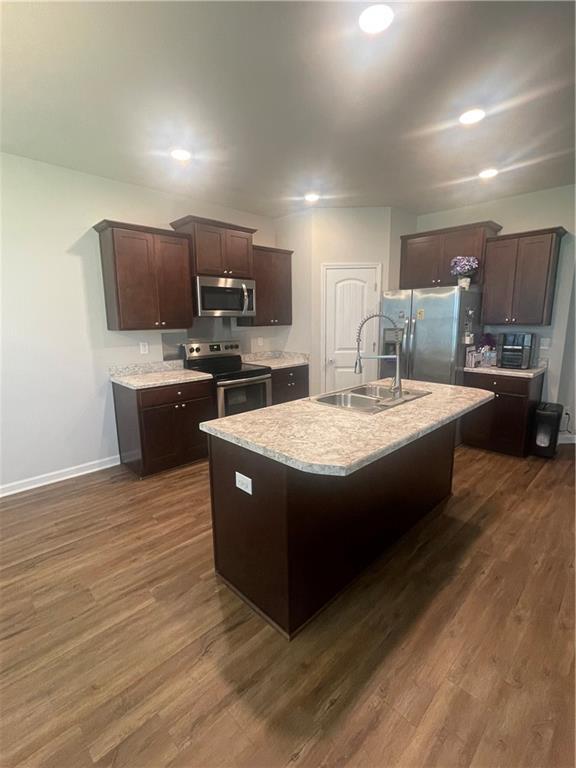 47715 Cathy Ln, Robert, LA 70455 - kitchen with appliances with stainless steel finishes, a sink, dark brown cabinetry, dark wood-style flooring, and a kitchen island with sink