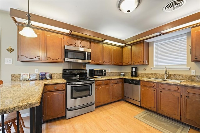 5705 Lafreniere St, Metairie, LA 70003 - kitchen featuring stainless steel appliances, a sink, light wood-type flooring, brown cabinets, and decorative light fixtures