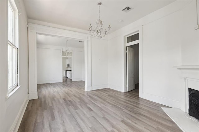 2305 Soniat St, New Orleans, LA 70115 - unfurnished living room with a chandelier, light wood-type flooring, a fireplace with raised hearth, and baseboards