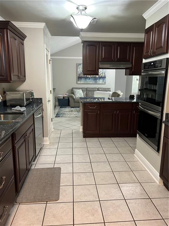 1705 Armagh Dr, Marrero, LA 70072 - kitchen featuring appliances with stainless steel finishes, light tile patterned floors, dark brown cabinetry, under cabinet range hood, and vaulted ceiling