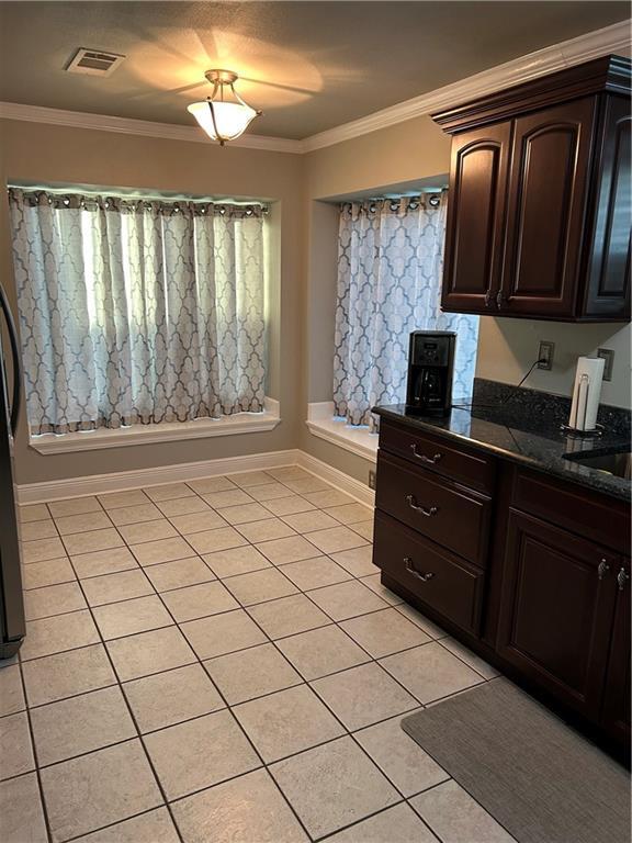 1705 Armagh Dr, Marrero, LA 70072 - kitchen featuring light tile patterned floors, dark brown cabinetry, crown molding, dark stone counters, and baseboards