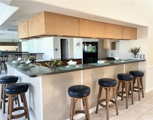 4231 San Trovaso St, New Orleans, LA 70129 - kitchen with light brown cabinets, dark countertops, a peninsula, and a kitchen bar