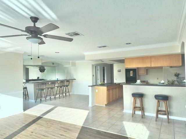 4231 San Trovaso St, New Orleans, LA 70129 - kitchen with dark countertops, a peninsula, a breakfast bar, ceiling fan, and crown molding