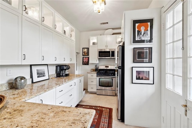 927 Dauphine St, New Orleans, LA 70116 - kitchen with appliances with stainless steel finishes, white cabinetry, light stone counters, and glass insert cabinets
