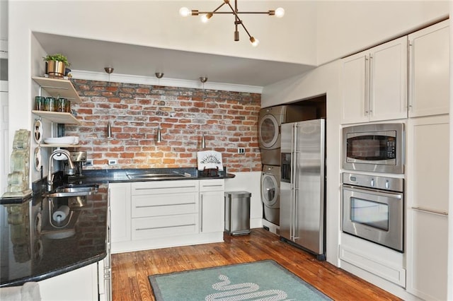 4716 Annunciation St Unit 3A, New Orleans, LA 70115 - kitchen featuring stainless steel appliances, stacked washing machine and dryer, dark countertops, dark wood-style flooring, and brick wall
