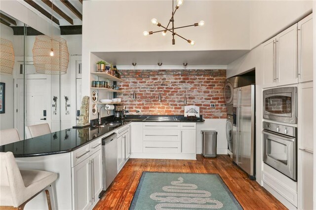 4716 Annunciation St Unit 3A, New Orleans, LA 70115 - kitchen featuring stainless steel appliances, stacked washer and clothes dryer, a chandelier, open shelves, and dark wood-type flooring