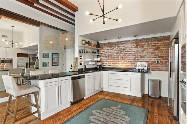 4716 Annunciation St Unit 3A, New Orleans, LA 70115 - kitchen with appliances with stainless steel finishes, a chandelier, a peninsula, brick wall, and dark countertops