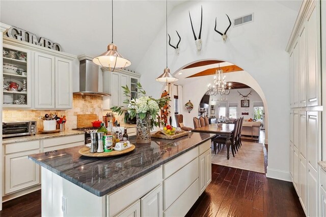 6838 Catina St, New Orleans, LA 70124 - kitchen featuring wall chimney exhaust hood, arched walkways, decorative backsplash, dark wood-style flooring, and dark stone countertops